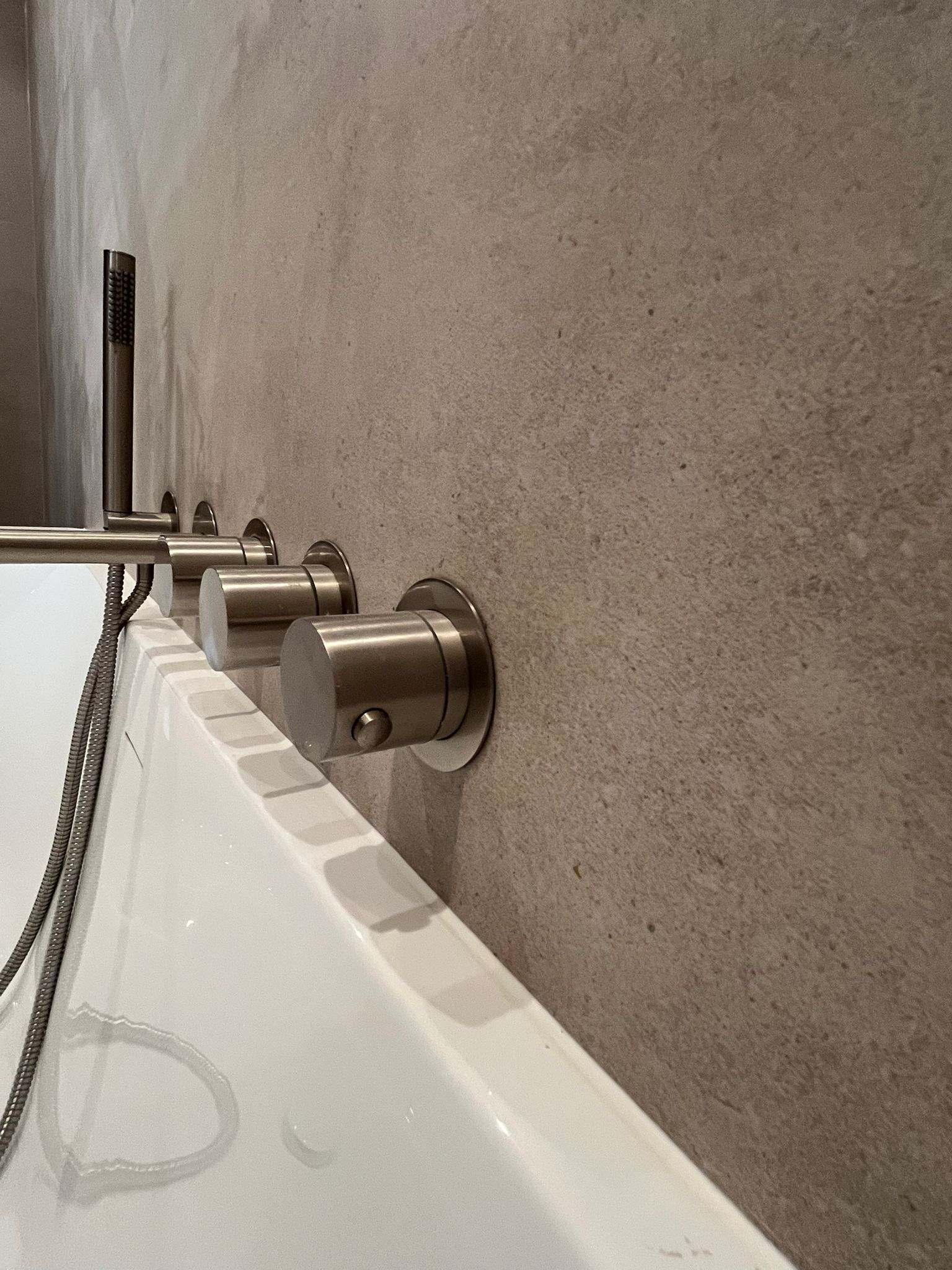 Wandgemonteerde geborsteld metalen kraan en handdouche boven wit bad