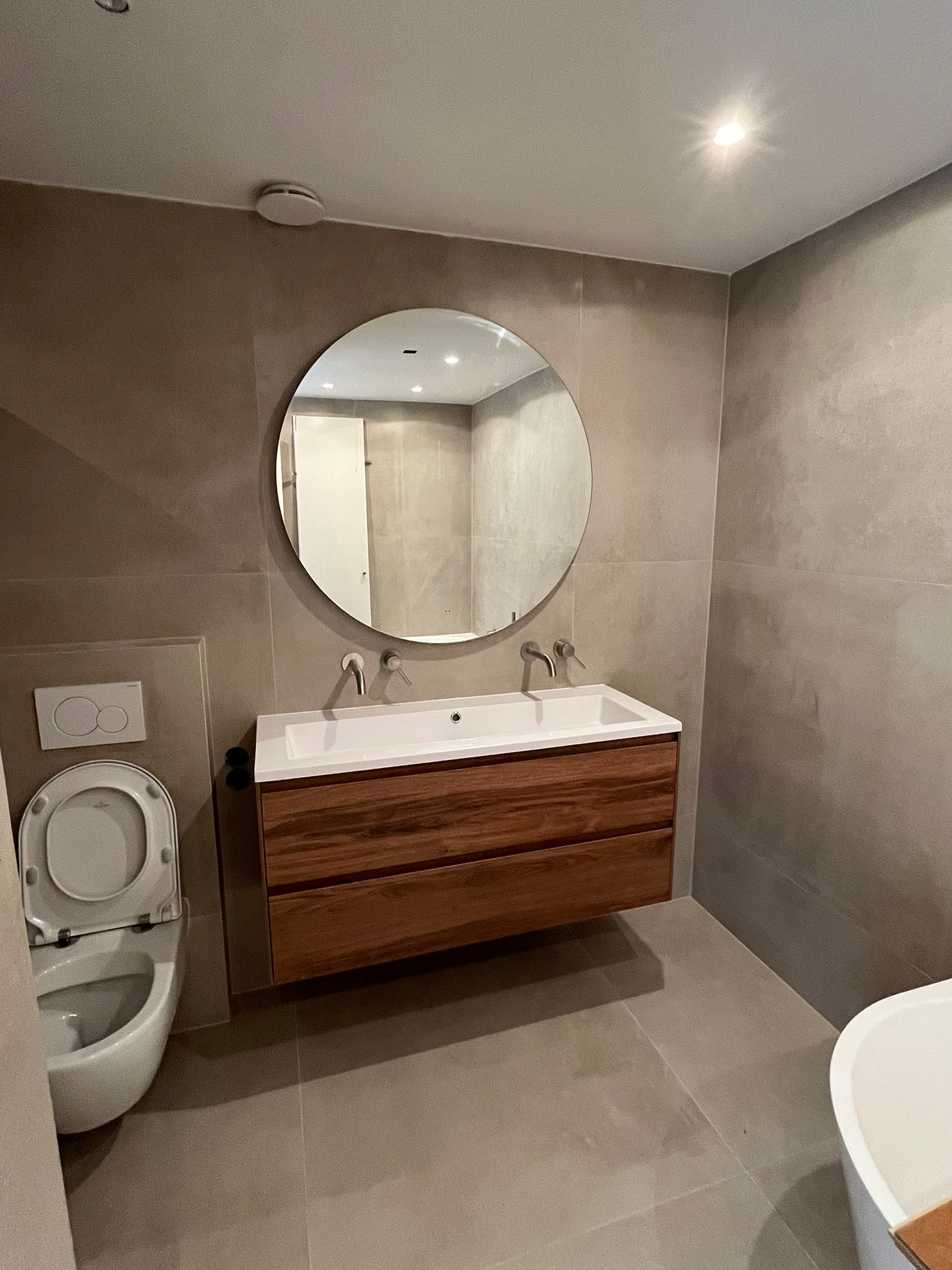 Badkameroverzicht met zwevend meubel, ronde spiegel en hangend toilet