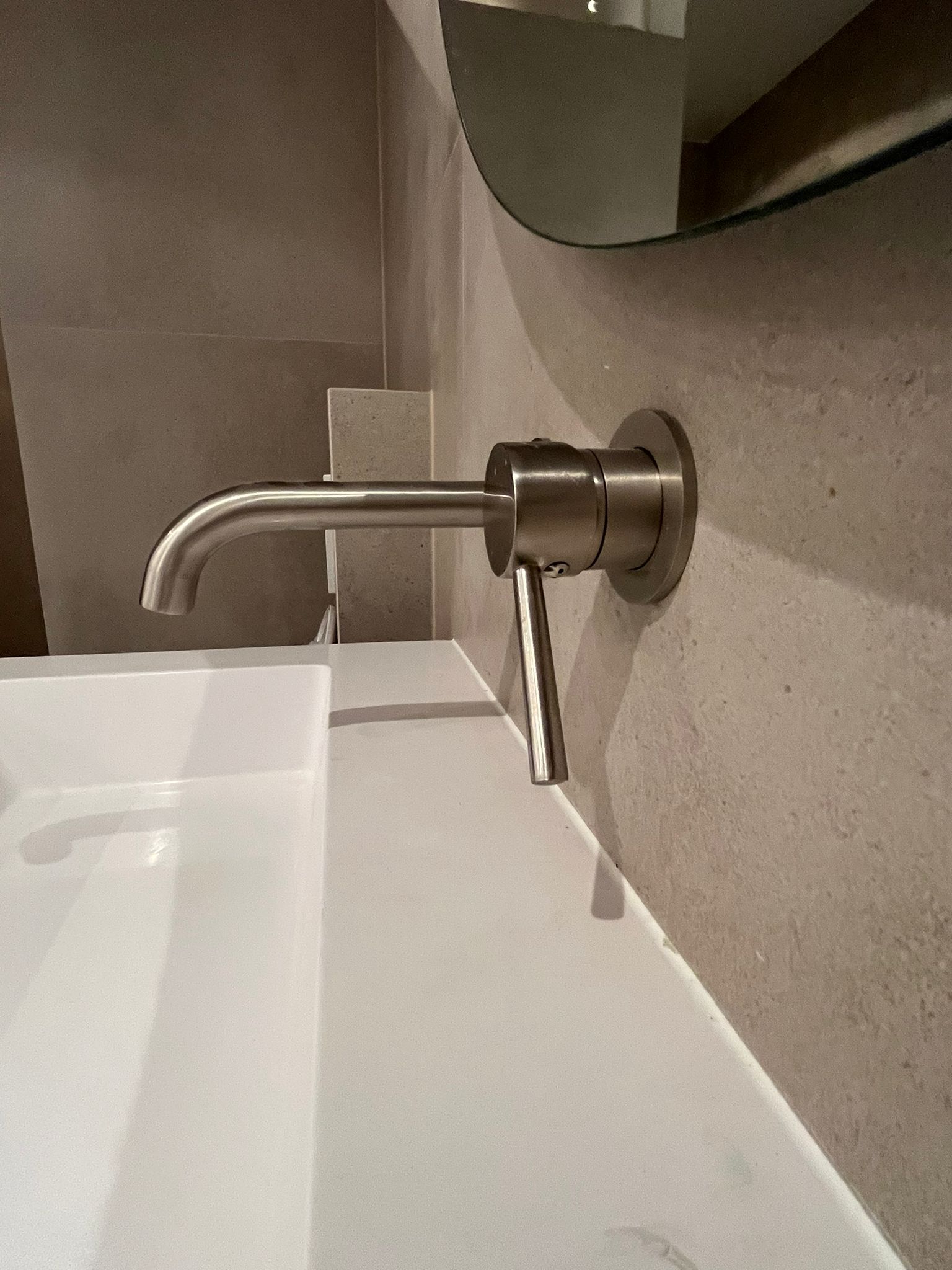 Wandgemonteerde geborsteld metalen kraan boven witte wastafel