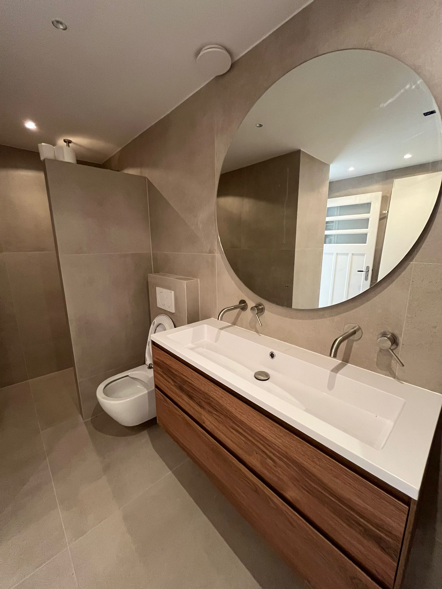 Gerenoveerde badkamer met zwevend walnoten wastafelmeubel, ronde spiegel en hangend toilet